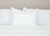 A neatly made bed features three Pillowtex Kyoto Pillows—Japanese style, half buckwheat and half polyester—upright against a light beige wall, creating a clean and minimalist look.