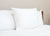 A Best Western® Everest Pillow by Keeco with soft polyester fill rests upright against a white headboard on a tidy bed, highlighting comfort and minimalism for those who want a restful, inviting space.